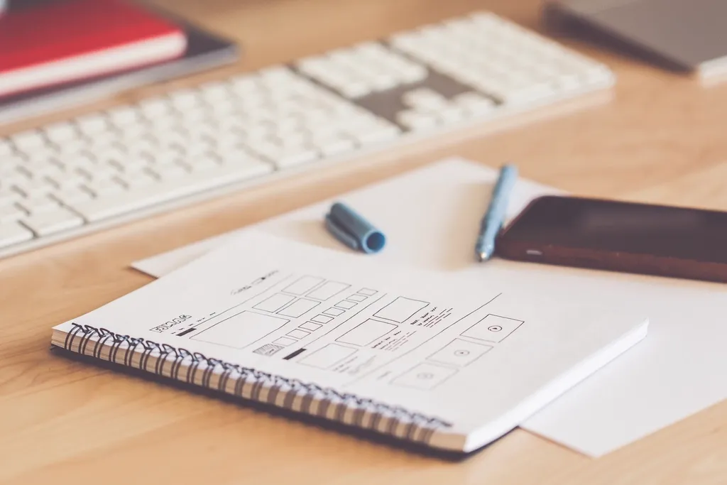 Web design process: wireframe sketches in a notebook on a desk beside a keyboard and phone